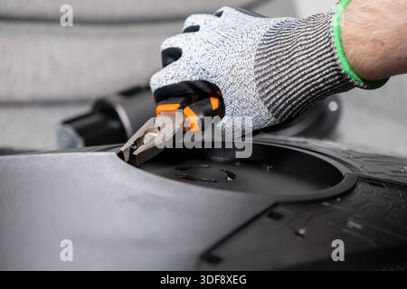 Close-up of worker's gloved hand using orange pliers to carefully assemble dark machine part, highlighting industrial repair and professional maintena Stock Photo