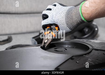 Close-up of a person's hand wearing a safety glove, carefully utilizing pliers to fix intricate internal components of a modern electronic device on a Stock Photo