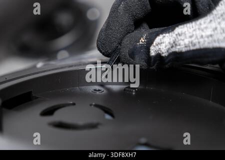 Top view of a professional's gloved hand meticulously placing a small threaded metal standoff into a black plastic electronic assembly, signifying pre Stock Photo