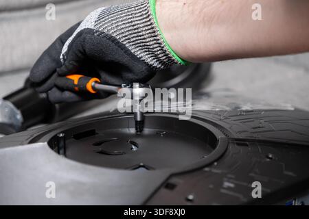 Gloved hand precisely using a small ratchet wrench to fasten a screw on a dark electronic device, showcasing meticulous technical repair and assembly Stock Photo
