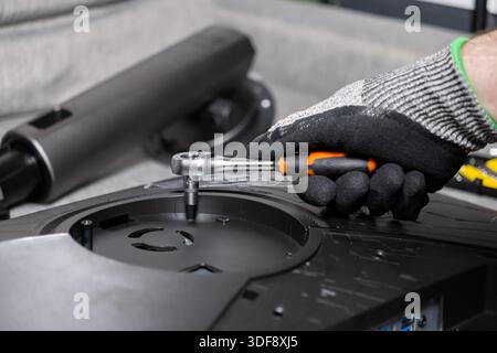 Detail of a gloved hand using a ratchet wrench for precise assembly or repair of electronic equipment, emphasizing meticulous technical maintenance an Stock Photo