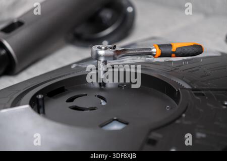 Close-up view of an orange-handled chrome ratchet wrench operating on a black plastic component, illustrating detailed manual work for maintenance and Stock Photo