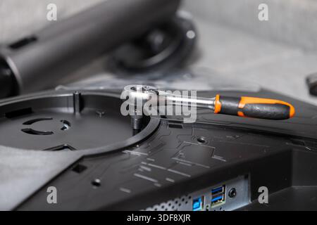 Professional silver ratchet wrench with orange grip placed on a black monitor's rear panel, illustrating technology setup, repair, and detailed electr Stock Photo