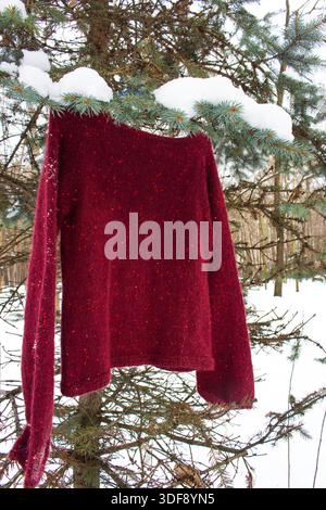Red knitted sweater with sequin hanging in winter park. Handmade fashion clothing. Burgundy sweater cardigan on winter snowy landscape. Stock Photo