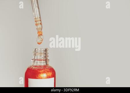 Cosmetic serum dropper above glass bottle with shimmering liquid Stock Photo
