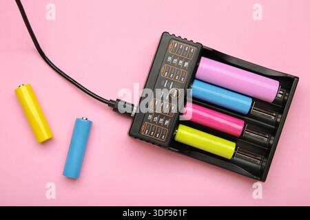 Rechargeable batteries in a battery charger on pink background. Four batteries in a charger. NI-MH and LI-MH battery. Stock Photo
