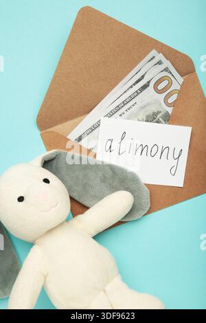 Toy bunny and envelope with word Alimony and money on blue background. Top view Stock Photo