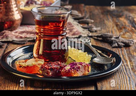 Tea in armudu glass with oriental delight rahat lokum on metal tray over wooden surface and tablecloth Stock Photo