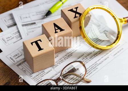 Indian Income tax return. The word "TAX" on wooden blocks. India. Files of documents to fill out. Magnifying glass, reading glasses, and pen.  Financi Stock Photo