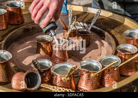 A man adds sugar to a copper coffee pot (cezve) while preparing Turkish sand coffee (kum kahvesi) in Sille near Konya, Turkey. Stock Photo
