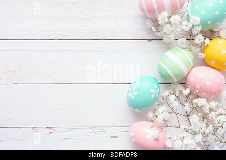 Pastel Easter eggs and white spring flowers. Above view side border against a white wood background. Copy space. Stock Photo
