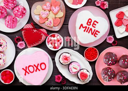 Valentines Day table scene with a selection of fun desserts and sweets. Above view on a dark wood background. Love and hearts theme. Stock Photo