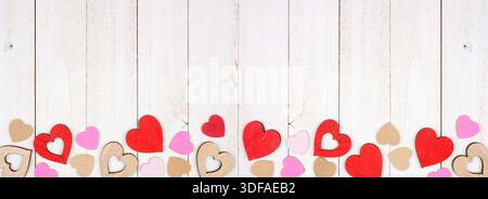 Valentines Day bottom border of wooden hearts. Top down view on a white wood banner background. Copy space. Stock Photo