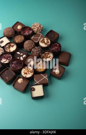 assorted artisanal chocolates and truffles clustered in a stylish flatlay on a mint-teal background, showcasing glossy ganache, nut and fruit toppings Stock Photo