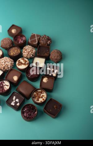 assorted artisanal chocolate pralines and truffles arranged diagonally on a teal backdrop, highlighting glossy and textured coatings, nut-topped ganac Stock Photo