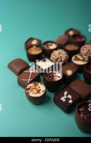 close-up of assorted gourmet artisanal chocolate bonbons and truffles arranged on a turquoise tabletop backdrop, showcasing glossy ganache shells, cre Stock Photo