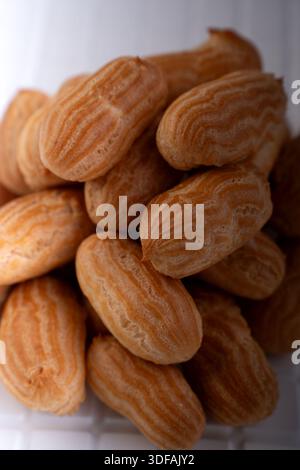 close-up pile of golden-brown choux pastries (mini éclairs) stacked on a white surface in a warm, inviting bakery-style scene, highlighting ridged toa Stock Photo