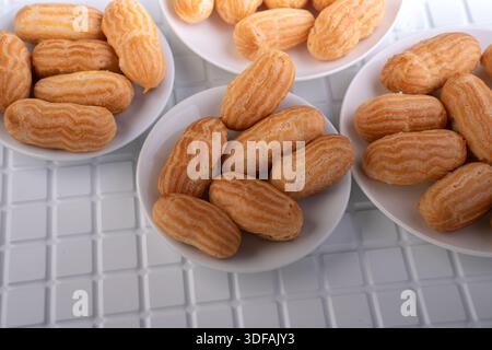 close-up view of golden mini eclairs neatly arranged in white porcelain bowls on a clean tiled tabletop, emphasizing ridged pastry texture, warm beige Stock Photo