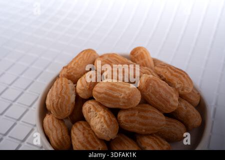 close-up of a piled bowl of small golden-brown choux pastries (mini eclairs) with ridged glazed shells on a white tiled tabletop, soft diffused studio Stock Photo