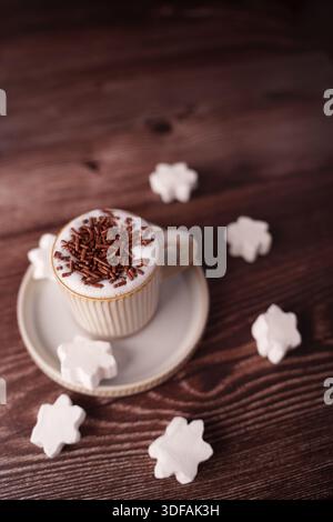 cozy warm coffee with chocolate sprinkles surrounded by festive star marshmallows on a wooden table evoking winter comfort and simple elegance in soft Stock Photo