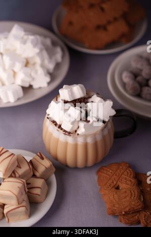 cozy winter treats with hot chocolate topped by marshmallows, surrounded by assorted cookies and sweets on a soft purple table setting, delight, sweet Stock Photo