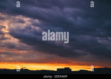 Dramatic storm clouds over fiery orange sunset city skyline silhouette, selective focus Stock Photo