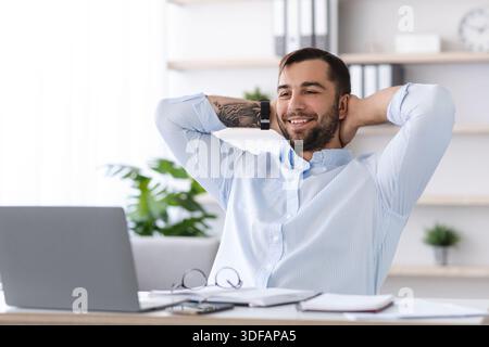 Smiling mature european male with beard take a break from work at laptop in office or living room Stock Photo