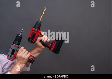 Two cordless drills held upright in hands, power tools with golden drill bits, red and black design, isolated background. Hands gripping two cordless Stock Photo