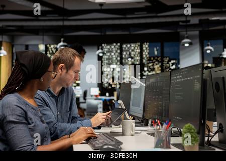 Manager assisting tech startup engineer coding advanced neural network algorithms during internship. Team leader helping african american trainee in office using deep learning models to do automation Stock Photo