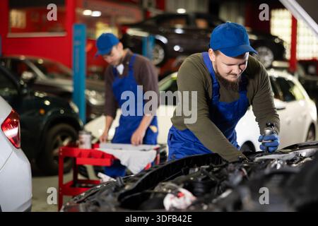 Professional mechanic man in uniform repairing car in auto repair garage Stock Photo