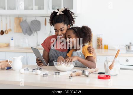 African american mother and daughter baking together, watching culinary blog Stock Photo