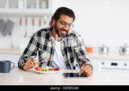 Positive arab guy having breakfast, using digital tablet, copy space Stock Photo