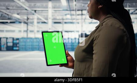 Software developer in data center using green screen tablet to ensure error free mainframes networks. Woman uses mockup device to monitor server hub gear parts for failures, camera A Stock Photo