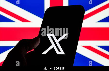 X logo on smartphone held in hand against blurred UK flag, concept of social networking, free speech debate and platform regulation. Stafford, United Stock Photo