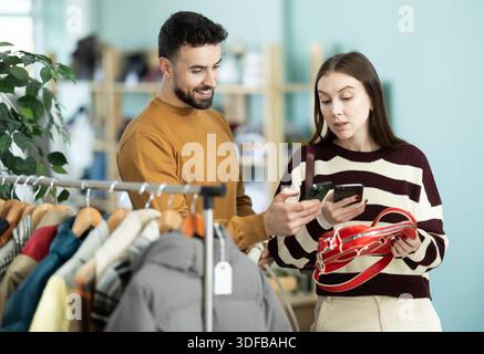 Woman selects handbag and checks its quality using QR code. Man helps her Stock Photo