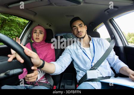 Nervous Muslim Lady In Hijab Having Driving Lesson With Instructor Stock Photo