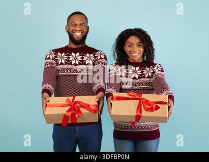 Happy african american couple stretching Christmas gifts to camera over blue studio background, celebrating New Year Stock Photo