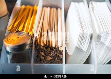 Organized restaurant condiment station with wooden stirrers, golden spoons, white plastic forks and a spice shaker in compartments, clean modern cafe Stock Photo