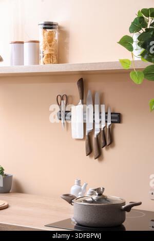 Magnetic holder with knives on light wall in kitchen Stock Photo
