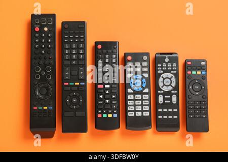 Different modern TV remote controls on orange background Stock Photo