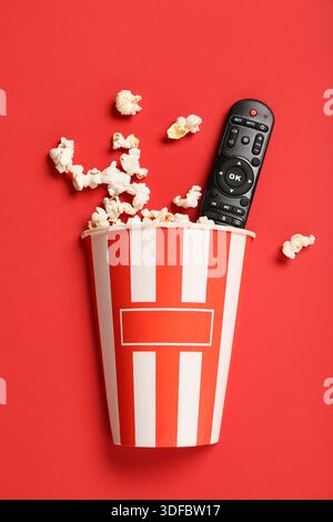 Bucket with modern TV remote control and popcorn on red background Stock Photo