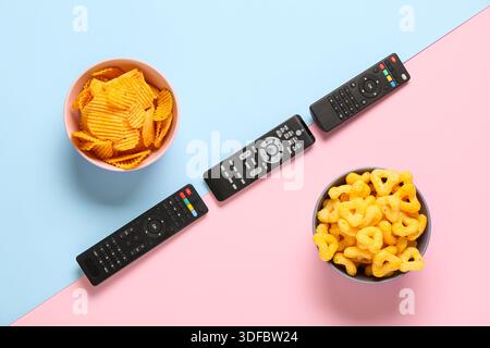 Different modern TV remote controls with bowls of crispy snacks on color background Stock Photo