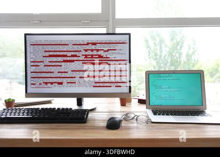 Computer monitor and laptop with programming code at programmer's workplace in office Stock Photo
