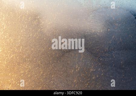 Golden sunlight on a frosty window creates a beautiful winter texture. Intricate ice patterns glitter, perfect for seasonal backgrounds and design Stock Photo