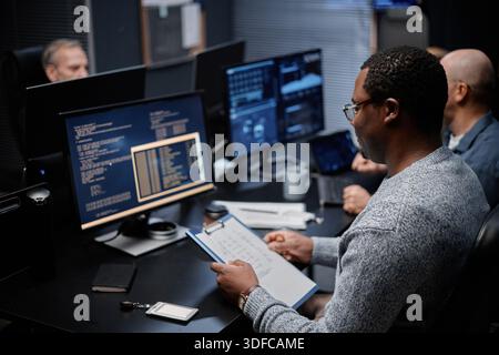 Young Adult Black Man Analyzing Data on Computer Monitors in Office Setting Stock Photo