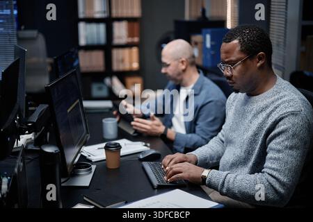 Middle Aged Black Man Working on Computer Beside Bald Caucasian Man Collaborating Stock Photo