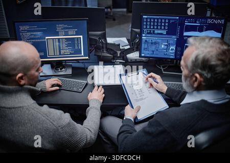 Middle Aged Caucasian Men Analyzing Cybersecurity Data on Computer Monitors Stock Photo