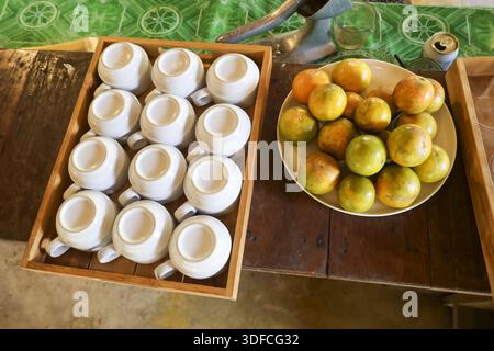 Top view of overturned white ceramic coffee cup in wooden tray near plate of fresh tangerine orange fruit on rustic wood table waiting for morning bev Stock Photo