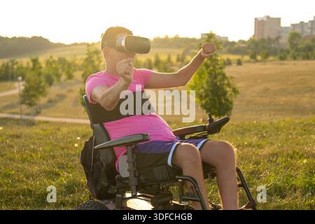 Businessman in wheelchair testing virtual glasses with updated program. Man enjoys playing VR games in sunlit meadow Stock Photo