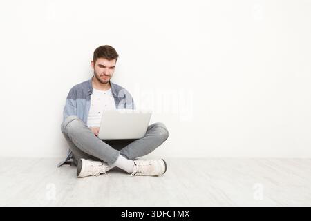 Young man working on laptop sitting on floor Stock Photo
